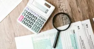 Calculator and magnifying glass beside tax forms for year end tax moves