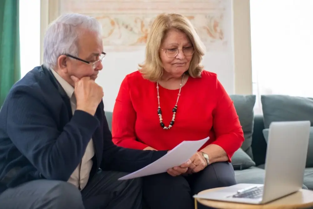 Older couple reviewing documents with a laptop open beside them