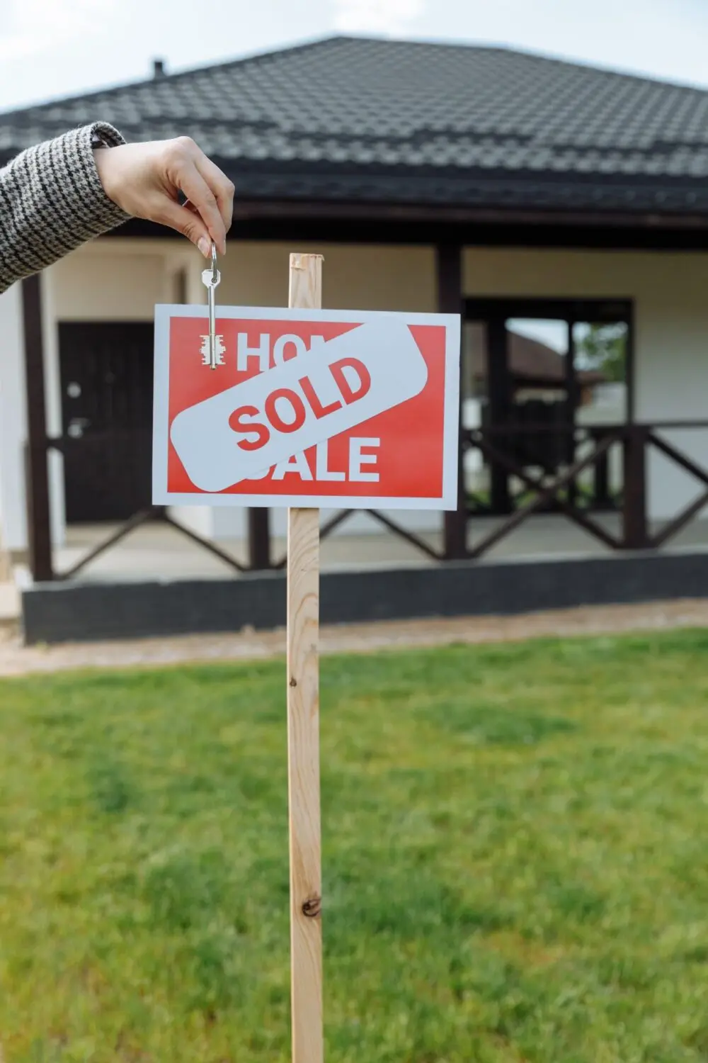 Hand holding a key next to a sold sign in front of a house