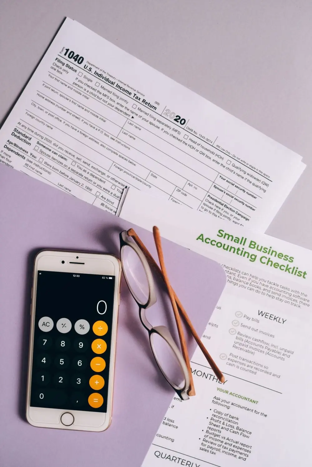 Phone calculator beside a small business accounting checklist and glasses
