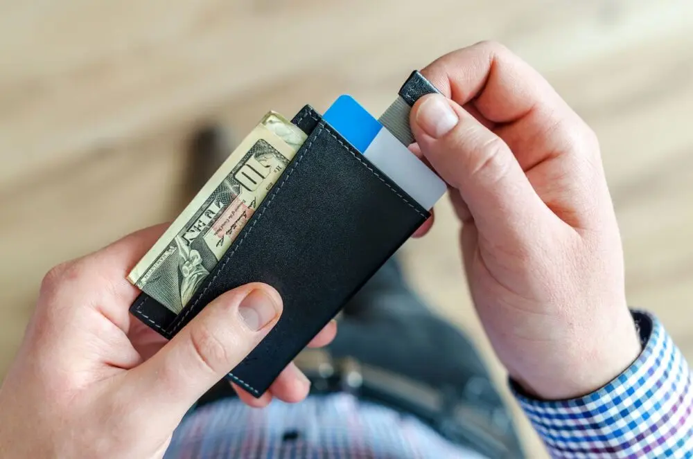 Hands pulling cash and cards from a slim wallet, a sign of how people pay and borrow in credit card earnings