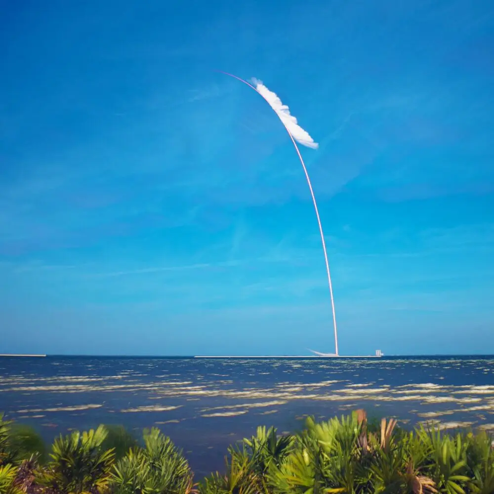 Rocket launch trail curving over water on a clear day