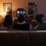 Three people seen from behind on a couch watching television in a living room