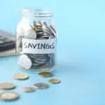 A glass jar of coins labeled Savings beside a calculator, illustrating the I bond rate decision