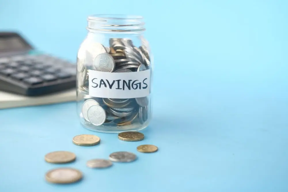 Savings jar with coins beside a calculator, used to compare savings rates
